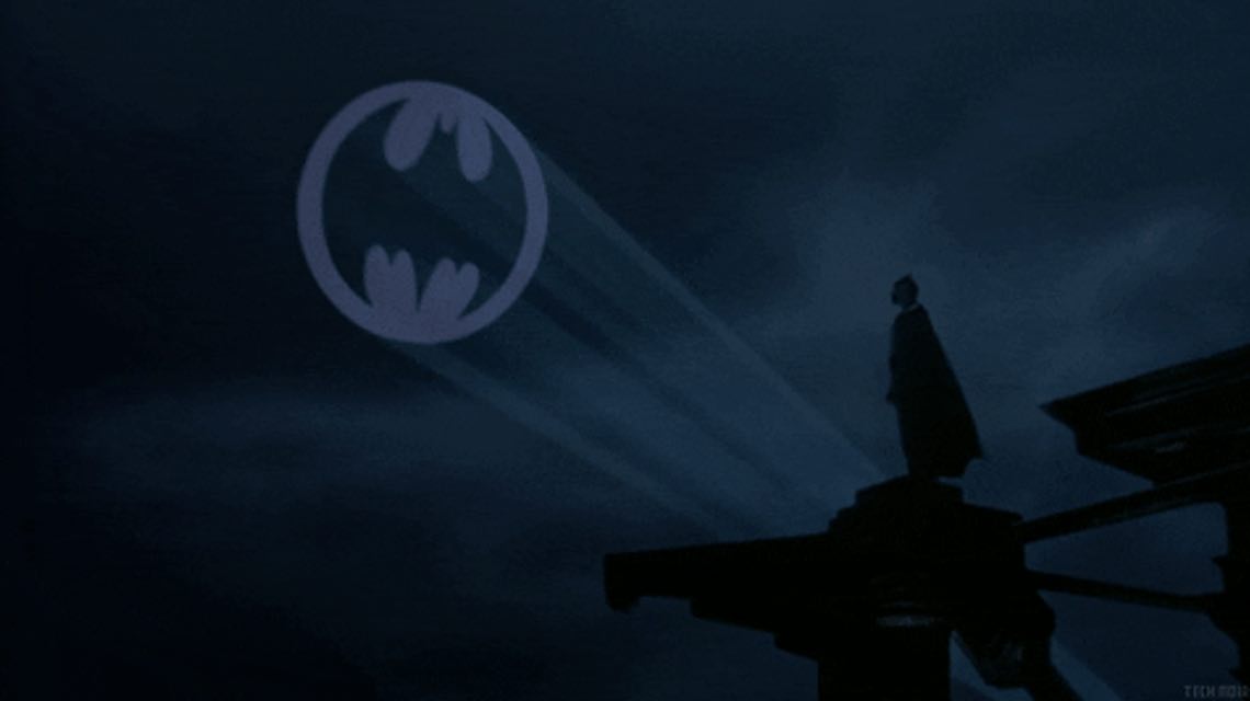 Batman stands on a roof, staring at the bat signal